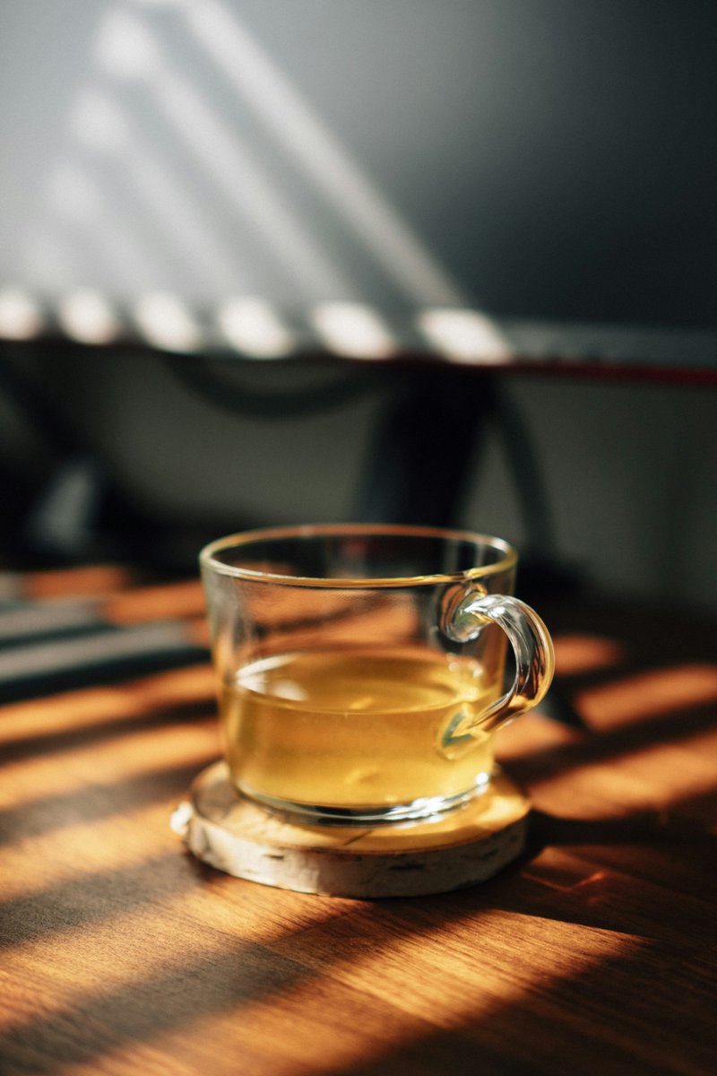 Tasse en verre remplie d'une infusion dorée, traversée par un rayon de lumière