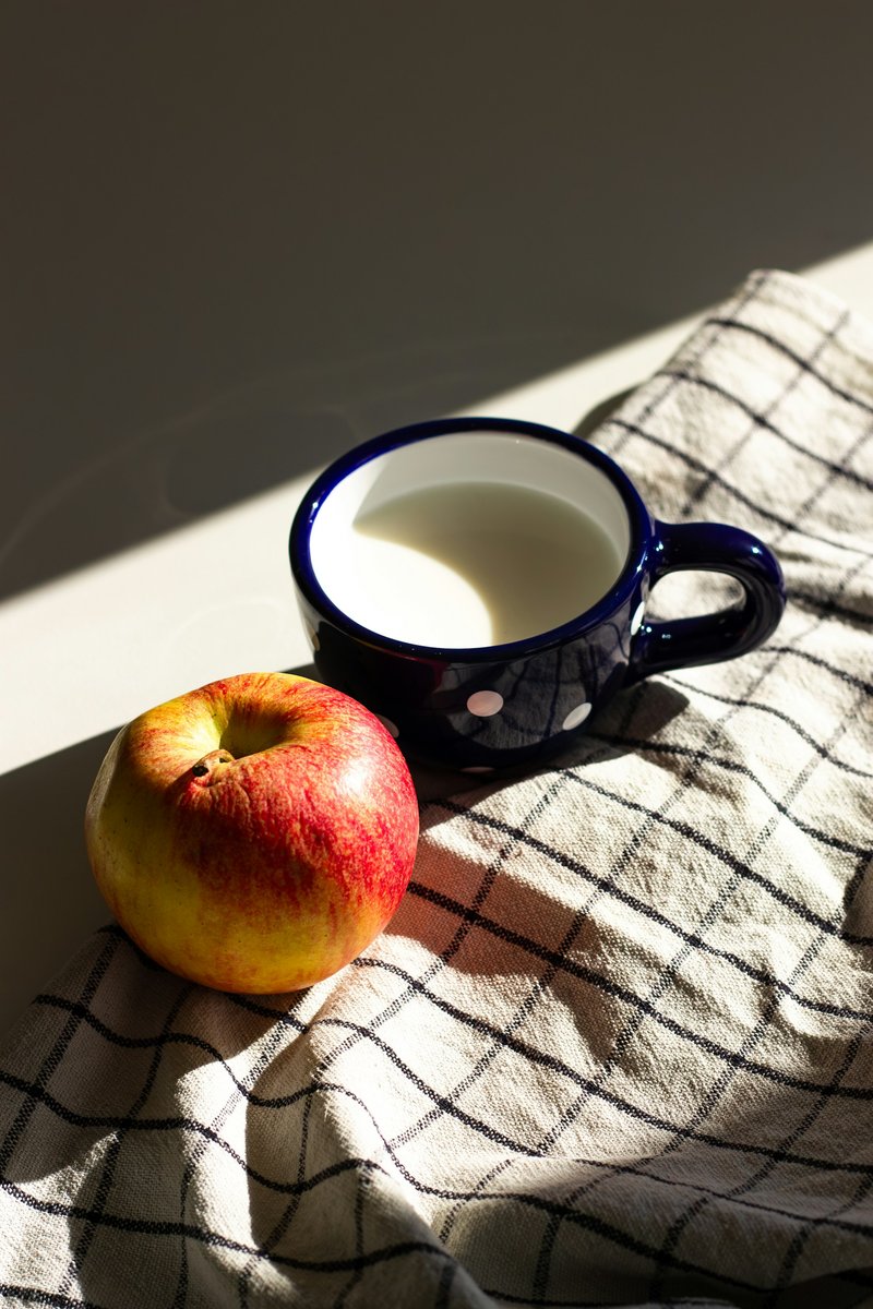 Tasse de lait posée à côté d'une pomme sur un torchon à carreaux