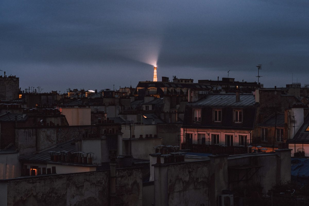 Toits de zinc et cheminées sous un ciel nocturne éclairé par la ville
