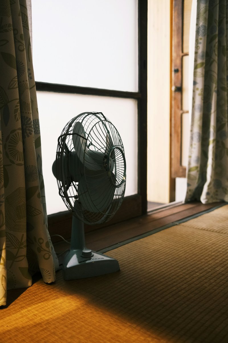 Ventilateur devant une fenêtre voilée, chaleur d'été