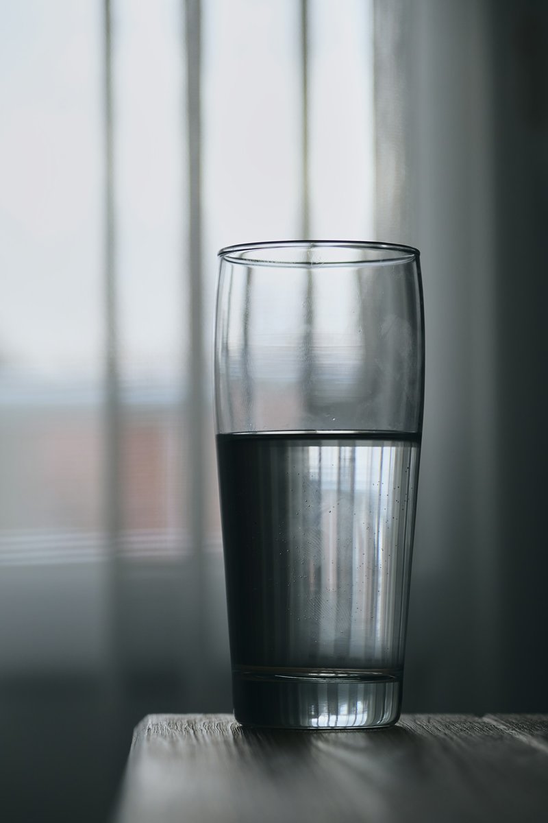 Verre d'eau posé devant un rideau, dans la lumière grise du soir